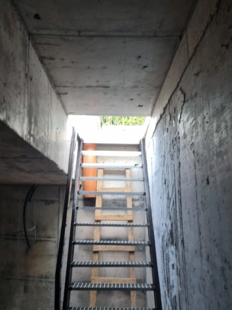 Interiorul unui beci terminat, cu scara metalică urcând spre trapa de acces și lumina de afară